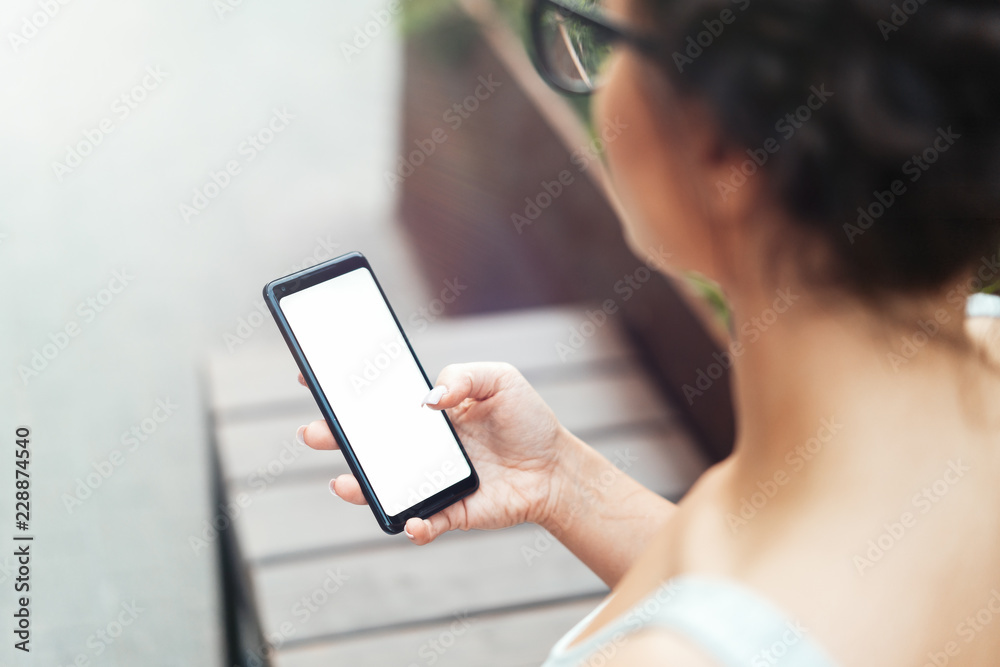 Young woman holding mobile phone with blank empty screen and texting message.