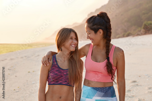 Overjoyed happy young females hug while have outdoor stroll  laugh and have fun  recreat in hot place against sandy beach  have positive expressions  good rest. People  emotions and lgbt concept