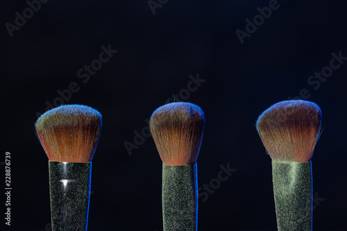 Mineral makeup and objects concept - Three makeup brushes with blue powder over dark background photo