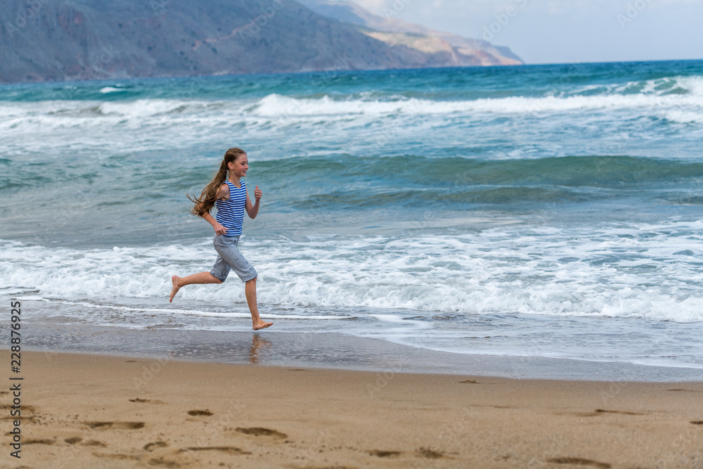 Cute happy little girl running along the beach in jumping over waves. Beautiful summer sunny day, blue sea, picturesque landscape. Cute happy little girl running along the beach in jumping over waves. Beautiful summer sunny day, blue sea, picturesque landscape.