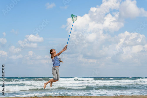 girl in a in striped t-shirt on the sea catches clouds by a net on a sunny day