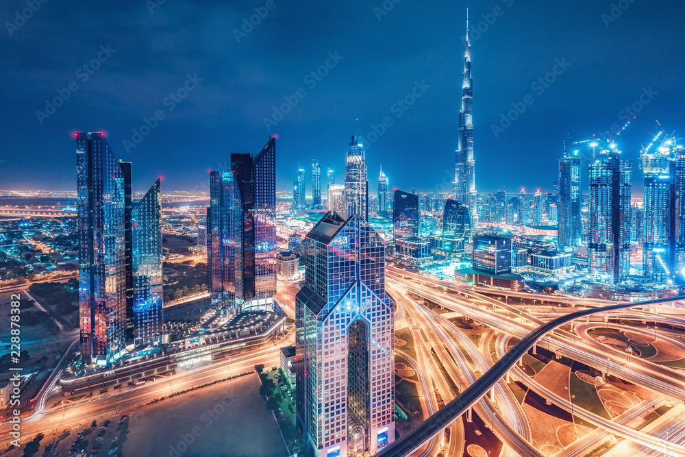 Fototapeta premium Spektakularna miejska panorama z kolorowymi iluminacjami miasta. Widok z lotu ptaka na autostrady i drapacze chmur w Dubaju, w Zjednoczonych Emiratach Arabskich.