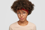 Unhappy dark skinned girl looks with displeased upset expression, frowns face, feels upset, wears glasses, casual sweater, isolated over white background. People and negative emotions concept
