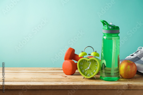 Fitness background with bottle of water, dumbbells and alarm clock
