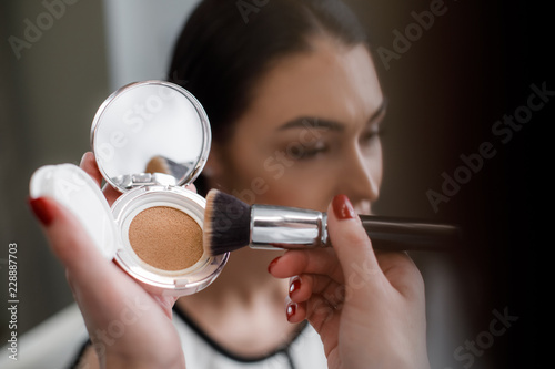 Close up of makeup artist using compact powder to matte skin and equalizing tone in beauty salon