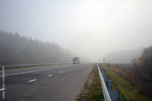 Truck is driving along the road in the morning in a thick fog