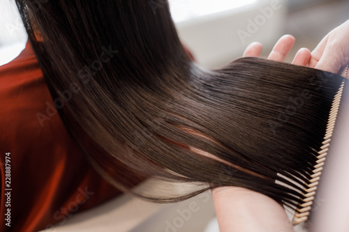 Close up. of beautiful silky hair is in hands of stylist while she combing by hairbrush
