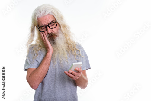 Studio shot of senior bearded man using mobile phone while looki