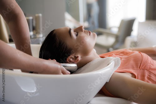 Tranquil lady is lying near sink and closing eyes. Master is washing her hair. Relaxing procedures for female in salon concept