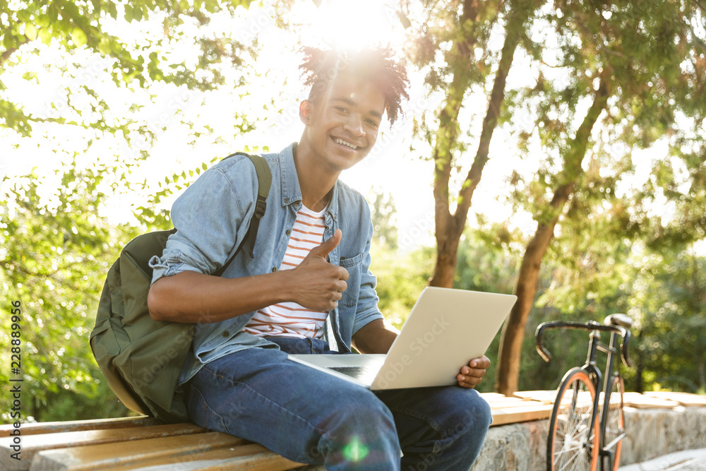 Emotional young african guy in park outdoors using laptop computer. Emotional young african guy in park outdoors using laptop computer.