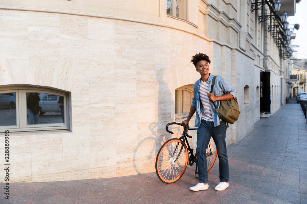 Happy young african guy walking with bicycle outdoors on the street. Happy young african guy walking with bicycle outdoors on the street.