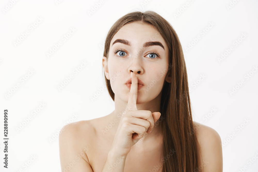 Close-up shot of tender and sensual feminine brunette female posing naked showing shhh gesture asking keep secret of beauty safe standing calm and soft over gray background hiding surprise Close-up shot of tender and sensual feminine brunette female posing naked showing shhh gesture asking keep secret of beauty safe standing calm and soft over gray background hiding surprise