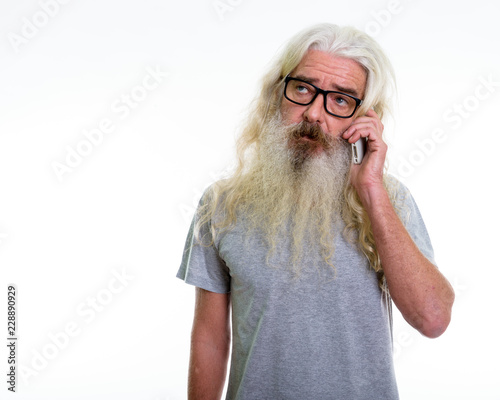Foto Studio shot of senior bearded man thinking while talking on mobi