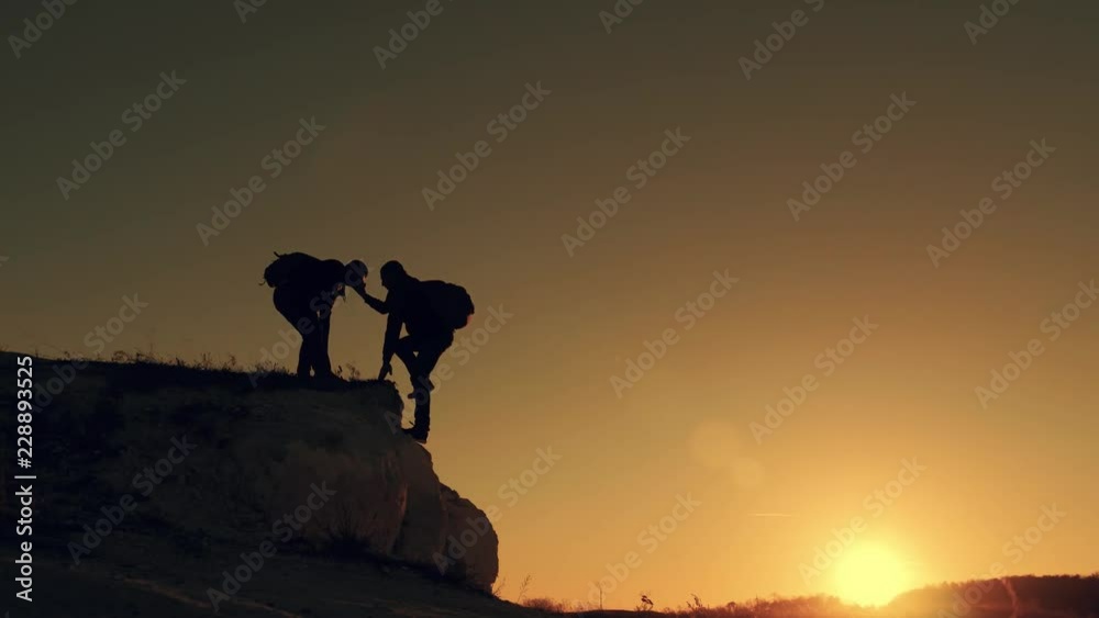 Silhouette of helping hand between two climber. two hikers on top of the mountain, a man helps a man to climb a sheer stone. couple hiking help each other silhouette in mountains with sunlight.