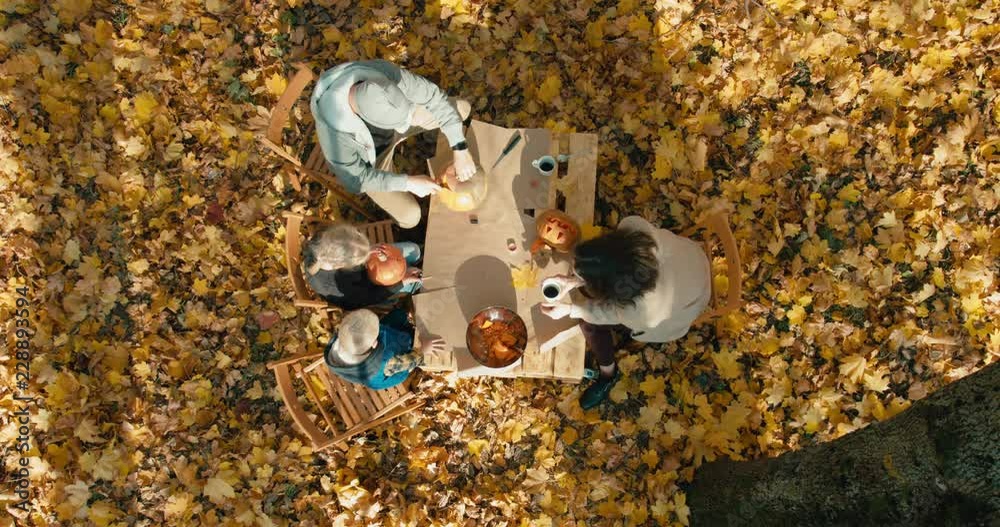 OVERHEAD CRANE Caucasian family - mother, father and 2 kids - boy and girl, carving pumpkins for Halloween on the table outdoors in the backyard. 4K UHD 60 FPS OVERHEAD CRANE Caucasian family - mother, father and 2 kids - boy and girl, carving pumpkins for Halloween on the table outdoors in the backyard. 4K UHD 60 FPS