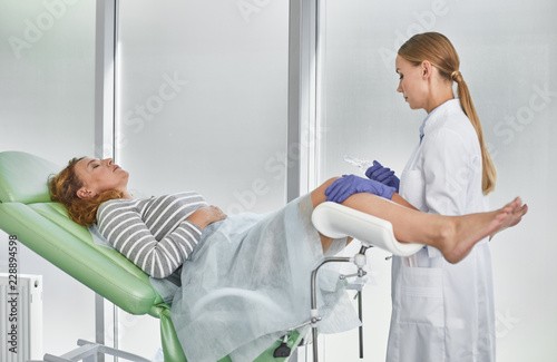 Фотография Side view portrait of young gynecologist in white lab coat and sterile gloves holding medical vaginal speculum