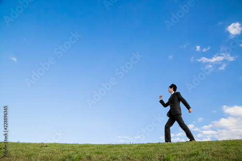 青空をバックに前進する若いビジネスマン1人。元気・成功・目標・挑戦イメージ © chikala