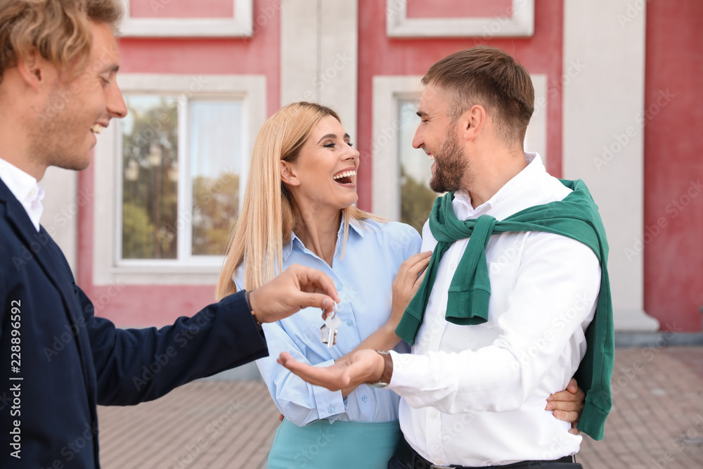 Fototapeta premium Male real estate agent giving house key to couple outdoors