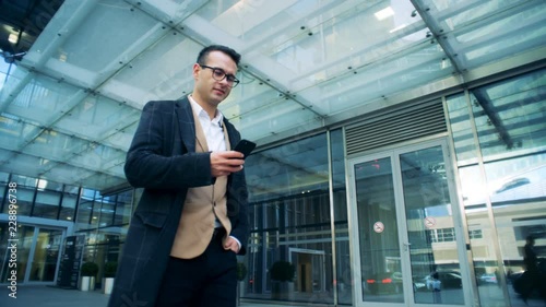 Wallpaper Mural Smiling manager is walking next to an office center with a smartphone. Red epic cinema camera shot. Torontodigital.ca