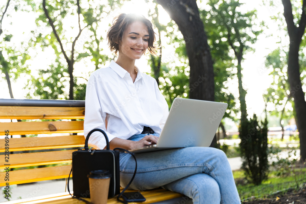 Smiling young woman sitting on bench outdoors Smiling young woman sitting on bench outdoors
