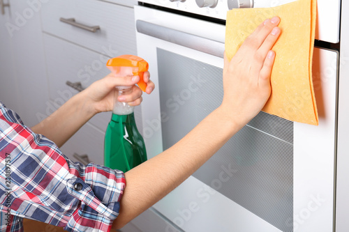 Woman cleaning electric oven with rag and detergent in kitchen, closeup