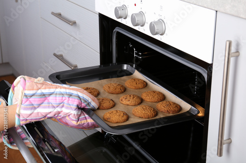 Woman taking baking tray with delicious cookies out of electric oven in kitchen, closeup