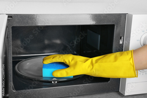 Woman cleaning microwave oven with sponge, closeup