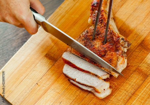 Chef hand with knife cutting meat on wooden board. photo