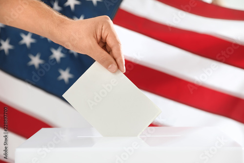 Man putting ballot paper into box and American flag on background, closeup