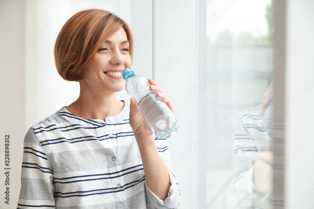 Woman drinking clean water from bottle at home. Space for text Woman drinking clean water from bottle at home. Space for text