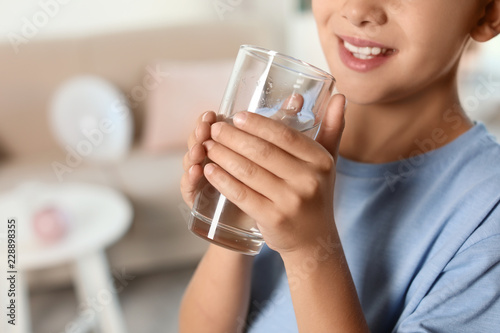 Little boy holding glass of fresh water at home, closeup