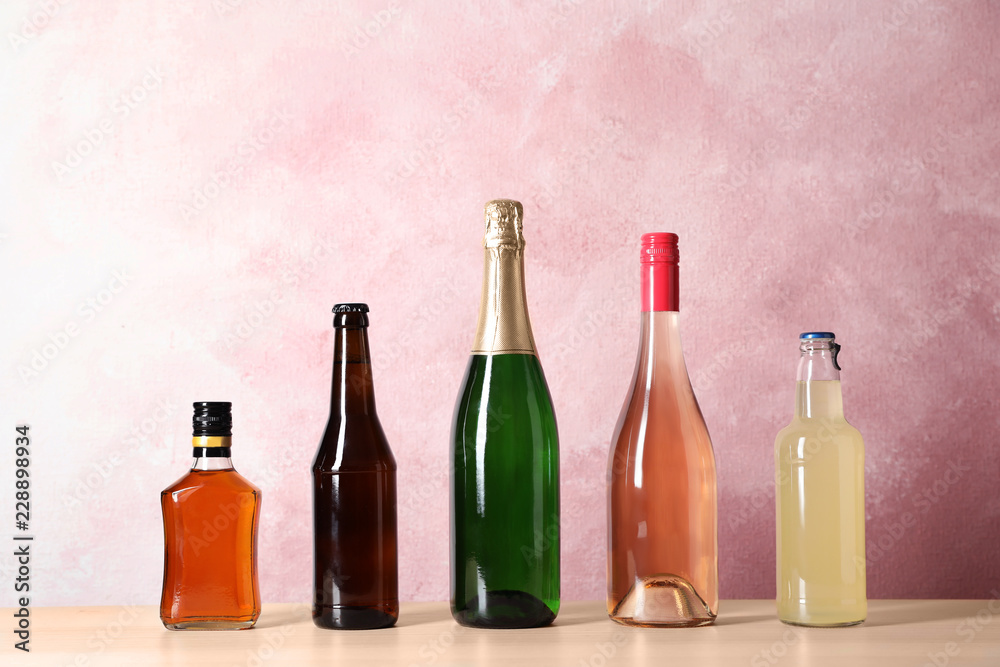 Bottles with different alcoholic drinks on table against color background Bottles with different alcoholic drinks on table against color background