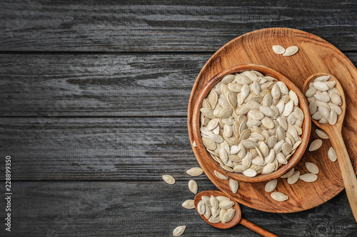 Raw pumpkin seeds in dish on wooden background, top view. Space for text