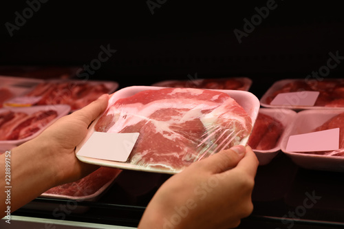 Woman taking packed pork meat from shelf in supermarket
