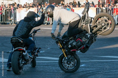 Two bikers perform motorcycle stunt riding Stoppie (Endo) trick photo