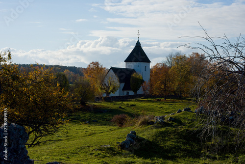Viking burrial feld with church from 1200s in Adelsö at lake Mälaren, Stockholm, a pale autumn day with blue sky and sea with clouds and orange leafs