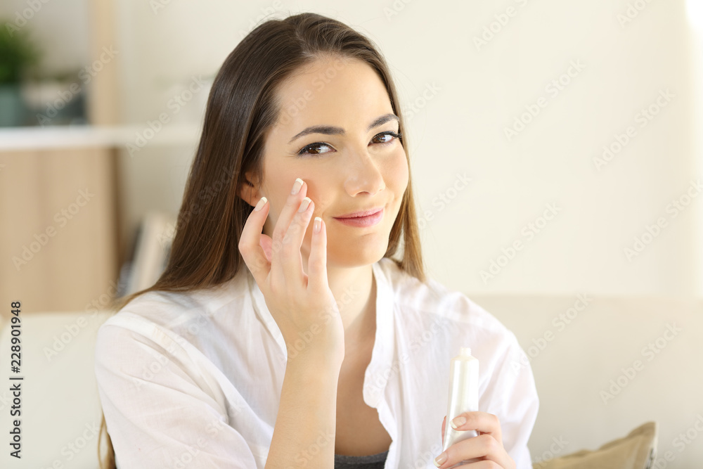 Relaxed woman applying moisturizer cream in cheek Relaxed woman applying moisturizer cream in cheek