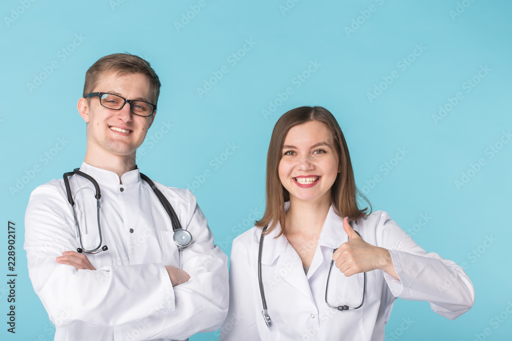 Two best smart professional smiling doctors workers in white coats showing thumbs up standing against blue background Two best smart professional smiling doctors workers in white coats showing thumbs up standing against blue background