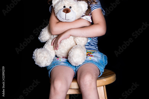 Beautiful little girl hugging a big bear bear. Portrait of little girl on black background. photo