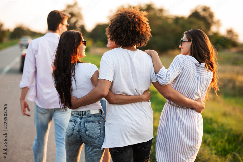 Back view. curly dark-haired young man hugging two girls. They talk and walk along the road. Back view. curly dark-haired young man hugging two girls. They talk and walk along the road.