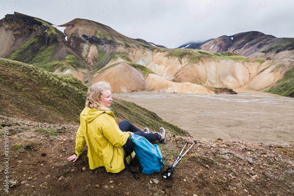 Fototapeta premium Woman in yellow raincoat overlooking the colourful mountains in Landmannalaugar national park, Iceland