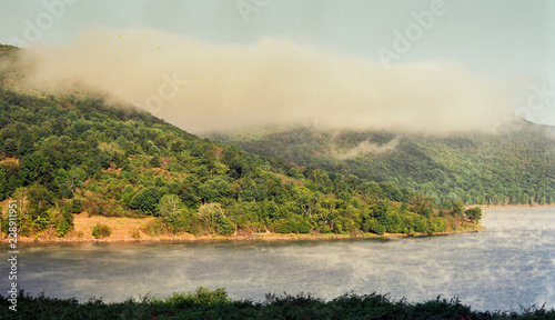 Cloud of fog hovers above hill and lake in summer 