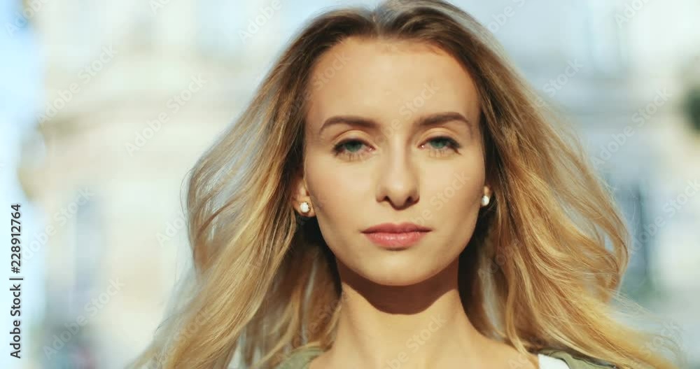 Portrait of the charming blonde young Caucasian woman smiling cheerfully to the camera. Outside. Close up. Portrait of the charming blonde young Caucasian woman smiling cheerfully to the camera. Outside. Close up.