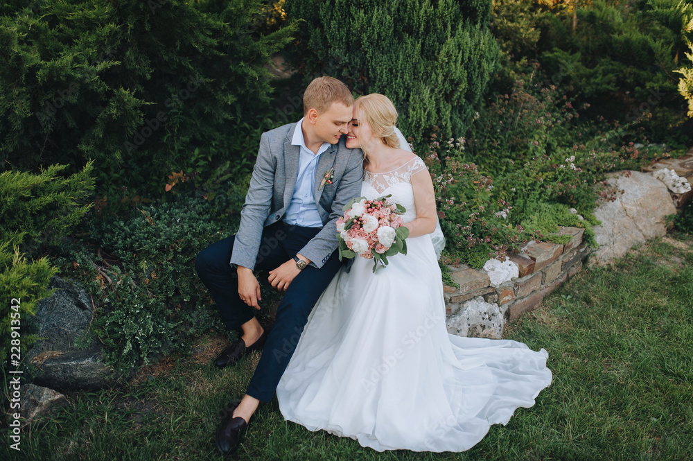 Beautiful newlyweds hugging in a green flowered garden, in nature and smiling. Wedding portrait of a stylish groom and young bride. Wedding photography.