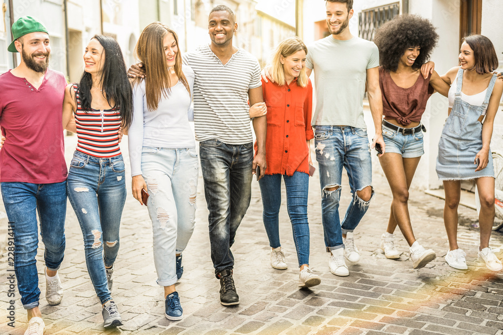 Fototapeta premium Multiracial millennial friends walking and talking in city center - Happy guys and girls having fun around old town streets - University students on travel vacations - Warm shadow filter tone