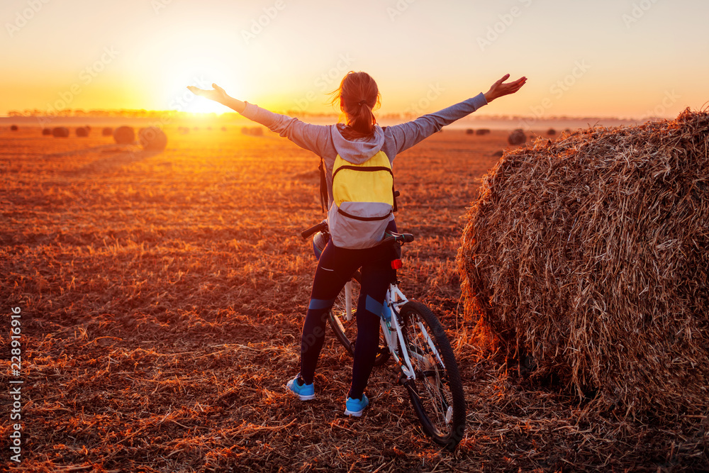 Obraz premium Happy young bicyclist raising opened arms in autumn field admiring the view. Woman riched destination.