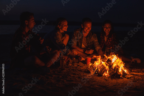 Camp on the beach. Group of young friends having picnic with bonfire. They are smiling
