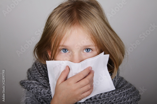 cute blond hair little girl blowing her nose with paper tissue. Child winter flu allergy health care concept