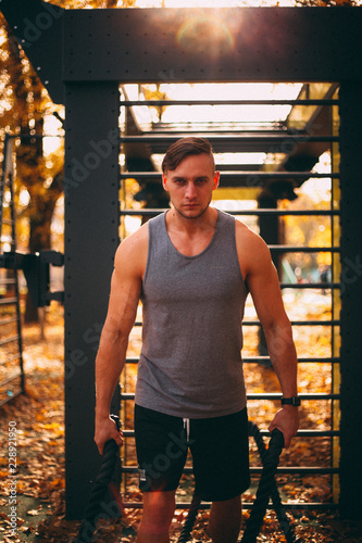 Young sexy athlete stands with a battle ropes against the background of the Wall bars in the park