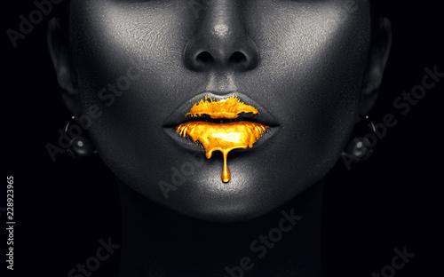 Gold paint drips from the sexy lips, golden liquid drops on beautiful model girl's mouth, creative abstract makeup. Beauty woman face isolated on black